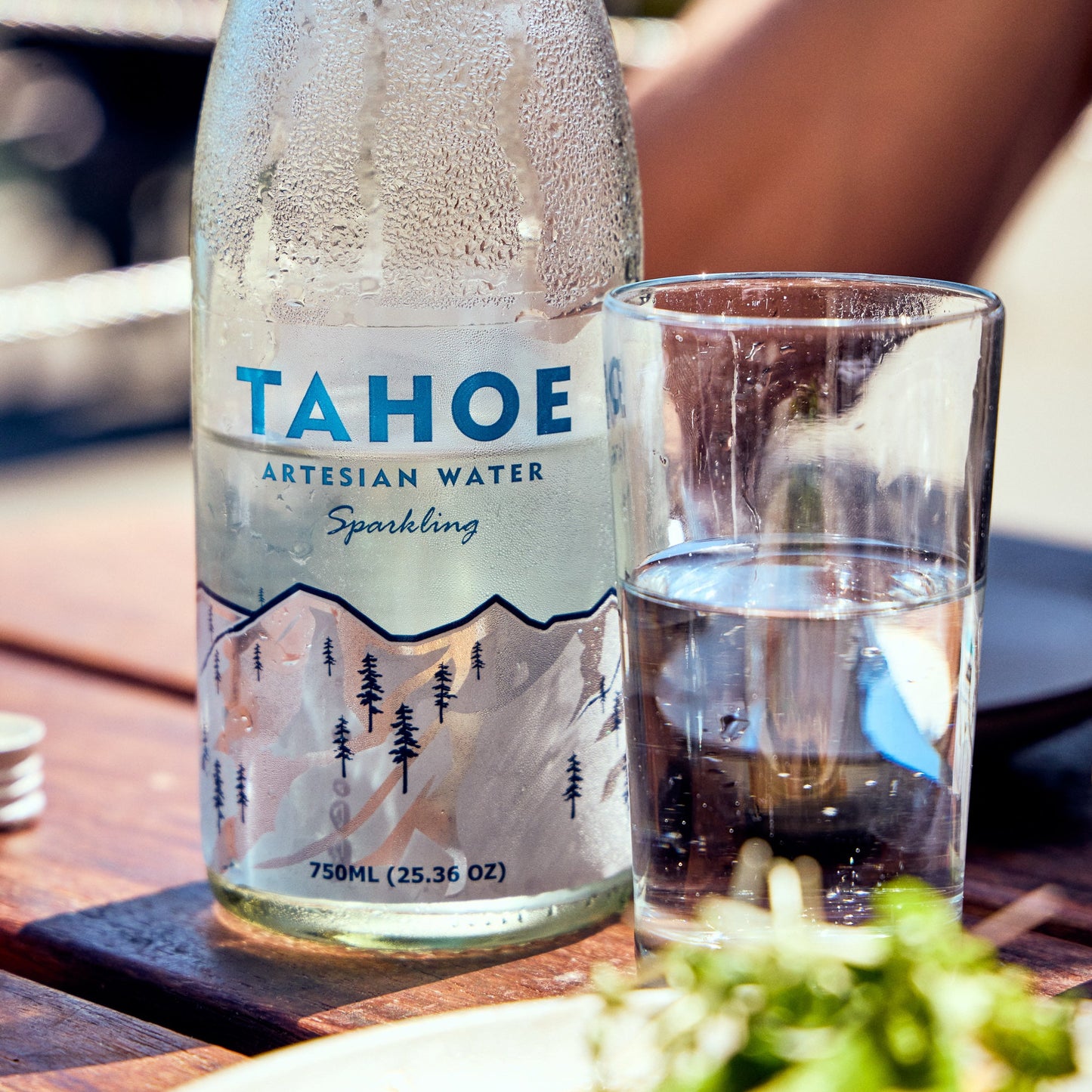 
                  
                    Bottle of Tahoe Artesian Water with a glass on a table outdoors
                  
                