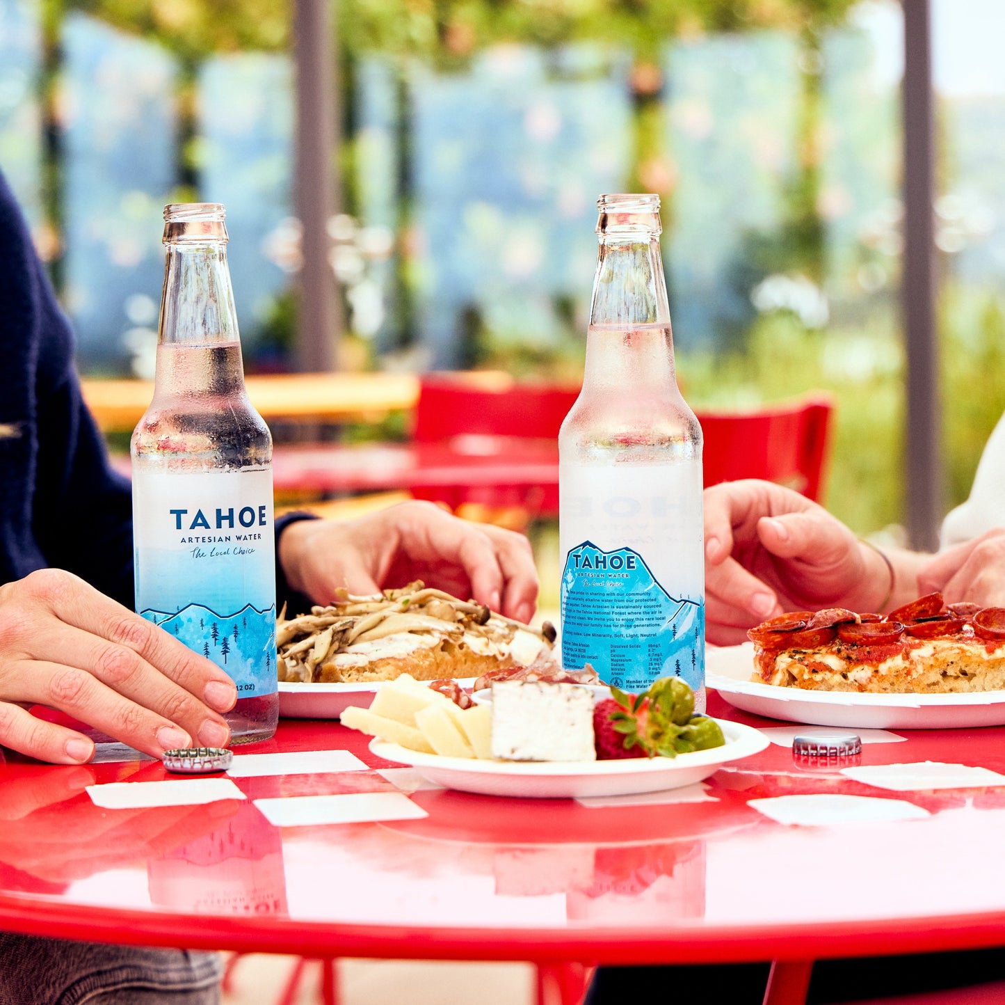 
                  
                    Two people sitting at a red table outdoors with plates of food and Tahoe brand bottles.
                  
                