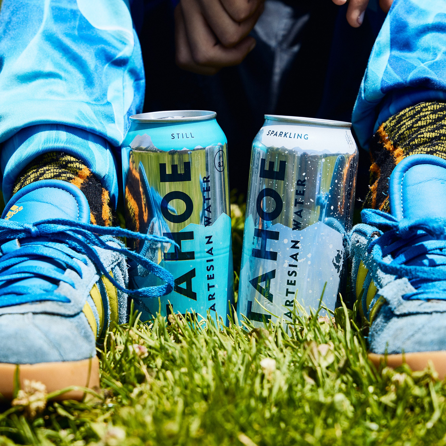 
                  
                    Person wearing blue shoes with cans of Tahoe Artesian Water on grass
                  
                